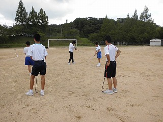 小学生と一緒に運動場でゴルフをしている生徒の画像