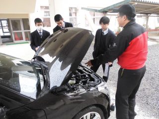 車のボンネットの中を見ながら教えてもらっている生徒の画像
